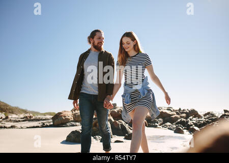 Beau couple strolling le long d'une plage de rochers. L'homme et la femme marcher avec la main dans la main sur la rive. Banque D'Images