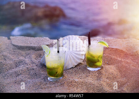 Boissons Mojito. Deux verres de mojito avec de la paille sur la plage avec vue sur l'océan. Coquillage blanc en arrière-plan. Le point de droit. Banque D'Images