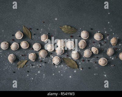 Schéma des pelmeni russes non cuits congelés avec des grains de poivre et les feuilles de laurier sur fond noir. Mise en page créative de boulettes. Belles matières dispersées quenelles. Vue de dessus ou de télévision. Banque D'Images