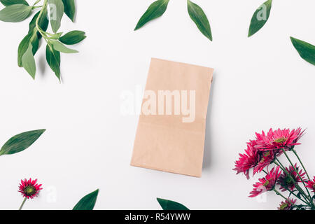 Sac de papier brun dans le centre de télévision jeter floral frame faite de feuilles vert frais et de floraison des fleurs roses sur fond blanc, vue du dessus. Banque D'Images