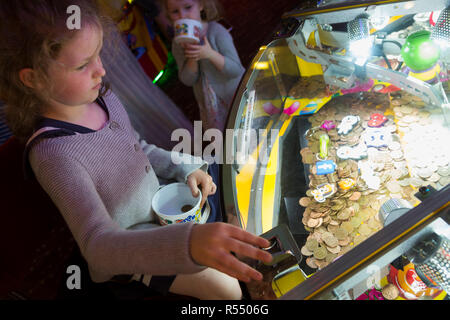 Jeune fille âgée de 6 ans / 6 ans jouant sur un coin pusher traditionnels populaires / pièces poussant en jeu pier arcade fun house. UK. (98). Banque D'Images