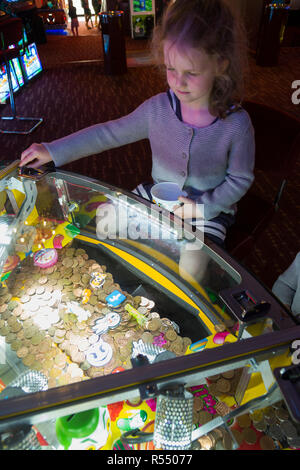 Jeune fille âgée de 6 ans / 6 ans jouant sur un coin pusher traditionnels populaires / pièces poussant en jeu pier arcade fun house. UK. (98). Banque D'Images