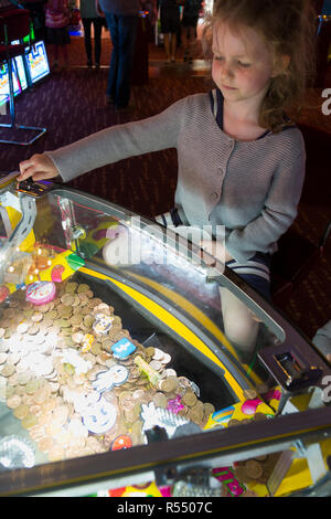 Jeune fille âgée de 6 ans / 6 ans jouant sur un coin pusher traditionnels populaires / pièces poussant en jeu pier arcade fun house. UK. (98). Banque D'Images