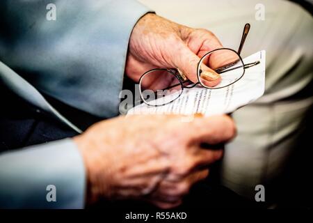 Gros plan sur les mains d'une femme âgée détient un document et une paire de lunettes. Banque D'Images