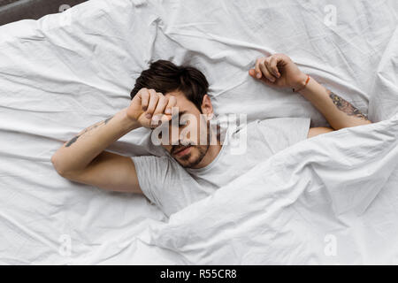 Vue de dessus du jeune homme dormir allongé sous couverture dans le lit à la maison Banque D'Images