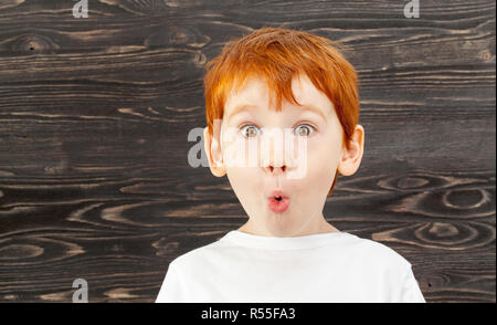 Portrait d'un enfant surpris avec des cheveux roux, des taches de rousseur et les yeux bruns, sur un fond noir Banque D'Images