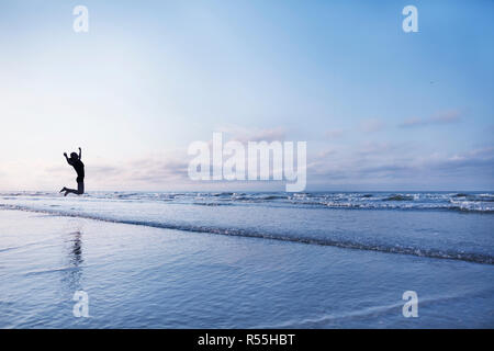 Femme sautant de joie sur la plage au lever du soleil Banque D'Images