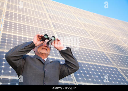 Businessman looking through binoculars en face de panneaux solaires Banque D'Images