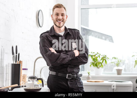 Smiling agent de police avec bras croisés debout à côté d'une table de cuisine Banque D'Images