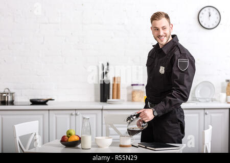 Smiling handsome policier verser du café de pot en verre cuisine à Banque D'Images