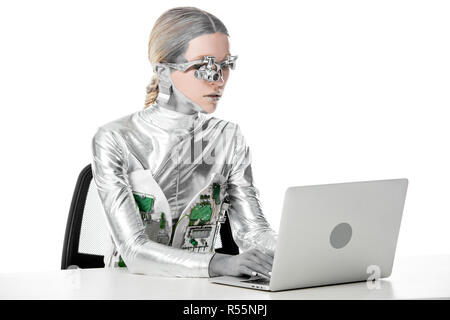 Robot d'argent assis à table et le travail avec ordinateur portable isolé sur blanc, avenir technologie concept Banque D'Images