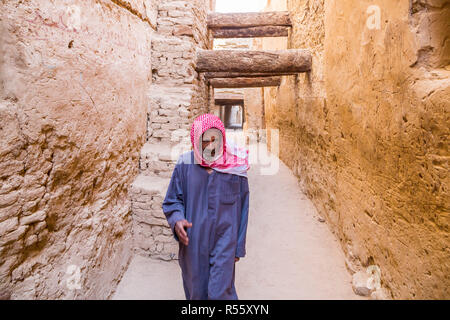 Dakhla Oasis, Egypte. Ancien égyptien arabe man walking habillé de bleu robe masculine nationale thawb, par l'intermédiaire de la rue médiévale, ville ancienne à Al Qasr. Banque D'Images