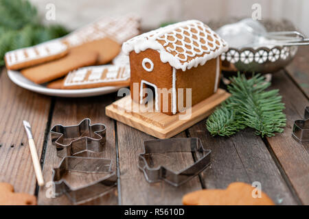 Jolie petite maison. Un grand nombre de biscuits au gingembre en forme différente sur table en bois brun. Décorées avec un glaçage sucré blanc. Matin d'hiver, l'humeur de Noël. Branches de sapin Banque D'Images