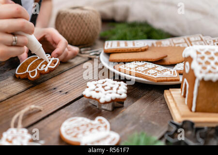 Une jeune fille décore ginger cookies sous la forme d'hiver Noël Bonhomme de matin. Cerise sur le miel attire femme gingerbread cookies. Table marron en bois. copier l'espace. Banque D'Images