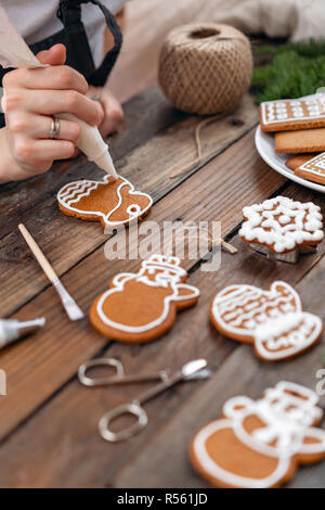Les cookies dans la forme de moufles. Une jeune fille décore ginger cookies hiver matin de Noël. Femme attire cerise sur le miel d'épices . Table marron en bois. copier l'espace. Banque D'Images