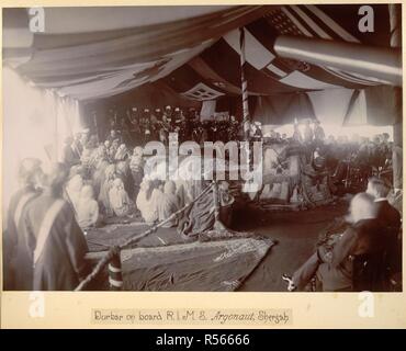 Jantes à bord Durbar, Shergah Argonaut [Sharjah ?]. Curzon et son personnel sont assis sur une estrade à l'extrémité de la terrasse devant un auditoire de fonctionnaires européens et arabes. Le pont est couvert d'un auvent de drapeaux. Collection Dane : 'Photographies de Lord Curzon's tour dans le golfe Persique, Novembre, 1903'. 1903 novembre. Photographie. Source : Photo 49/1(7). Langue : Anglais. Auteur : Inconnu. Banque D'Images