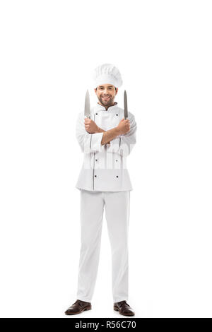 Beau jeune chef holding des couteaux à bras croisés et smiling at camera isolated on white Banque D'Images