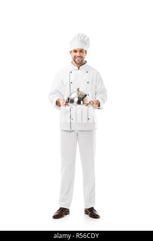 Beau jeune chef holding plateau de service avec dome et looking at camera isolated on white Banque D'Images