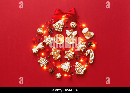 Bal de Noël créative faite de biscuits au gingembre glacé, l'anis étoile, petits fruits, orange, décoré d'un ruban rouge noeud sur fond rouge. Carte de voeux Nouvel An concept. Vue d'en haut. Banque D'Images