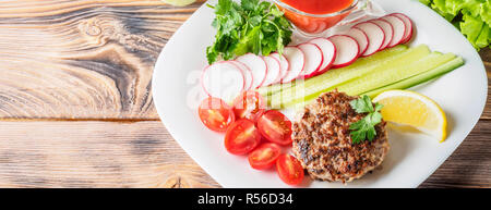 Steak haché escalope cuite au grill sur plaque blanche avec mélange assorty radis Légumes Tomates cerises tranches de concombres citron persil et sauce ket Banque D'Images