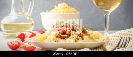 Les pâtes italiennes Penne bolognaise rigatone la viande hachée à la sauce tomate et de parmesan. Nature morte sur table en bois blanc, servi avec des tomates cerises, Banque D'Images