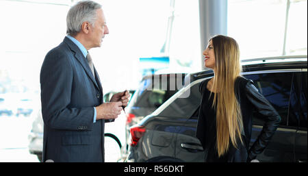 Portrait d'un vendeur de voiture en donnant des clés de voiture pour jeune femme debout à côté de la voiture de luxe brillant blanc dans electronics store Banque D'Images