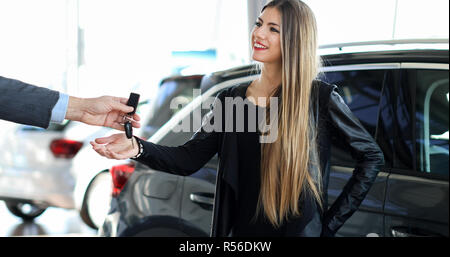 Portrait d'un vendeur de voiture en donnant des clés de voiture pour jeune femme debout à côté de la voiture de luxe brillant blanc dans electronics store Banque D'Images