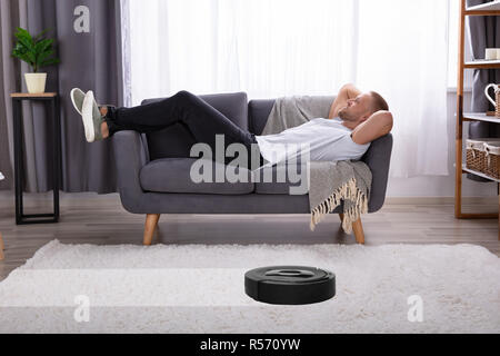 Young Man Aspirateur Robot sur un tapis Banque D'Images