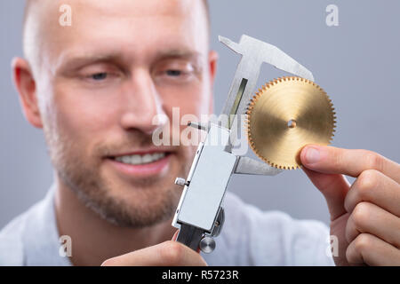 Portrait d'un homme mesurant la taille d'Engrenage avec pied à coulisse électronique numérique sur fond gris Banque D'Images