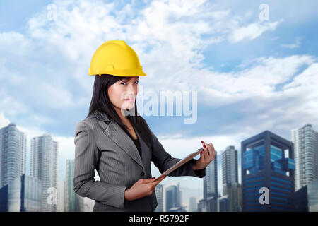 Smiling asian woman entrepreneur avec casque jaune holding clipboard Banque D'Images