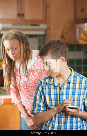 Teen boy se cache un message sur son téléphone mobile de curieux mère Banque D'Images