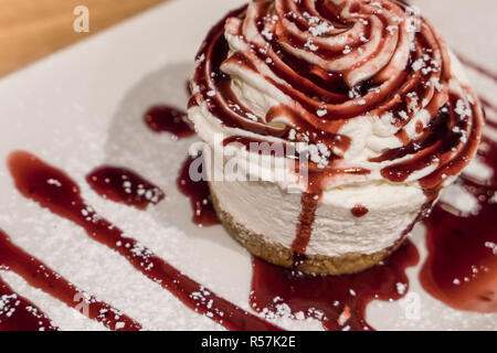 Petite ronde gâteau au fromage avec sauce pour fruits des bois, avec une pincée de sucre en poudre. Banque D'Images