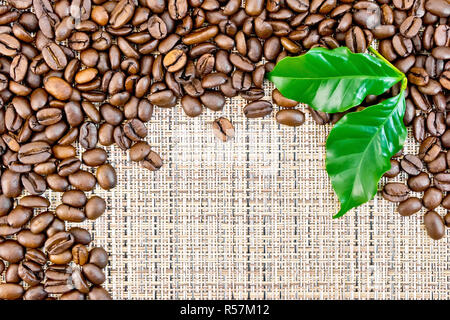 Les grains de café noir avec la feuille sur le tissu marron Banque D'Images