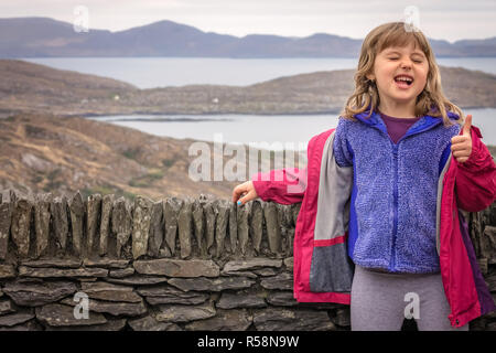 Cute little woman giving Thumbs up pour le beau paysage marin côtier dans le comté de Kerry le long de l'Anneau du Kerry, Irlande Banque D'Images