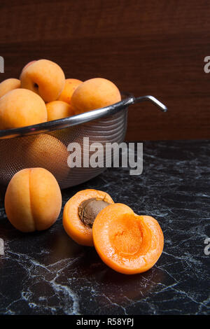 Organique mûres les abricots dans une passoire en acier. Composition dans un style rustique - jaune bio abricots juteux dans son ensemble et passoire en acier et des moitiés d'abricots o Banque D'Images