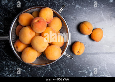 Organique mûres les abricots dans une passoire en acier. Composition dans un style rustique - jaune bio abricots juteux dans son ensemble et passoire en acier et des moitiés d'abricots o Banque D'Images