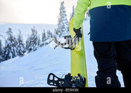 Vue arrière de l'escalade livres avec son conseil sur la montagne de l'arrière-pays de session freeride dans la forêt. Man with snowboard marche à ski resort. Rider à la mode de chaux tenue. Banque D'Images