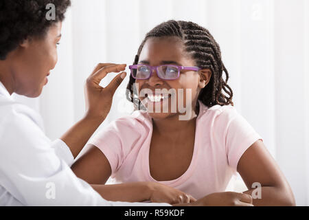 Smiling Girl Wearing Eyeglasses en face d'optométriste Banque D'Images