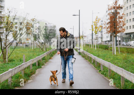 Un homme et son petit chien pratiquent 'walking à talon' dans le parc Banque D'Images