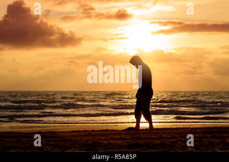 Homme marche et pense au coucher du soleil sur la plage Banque D'Images