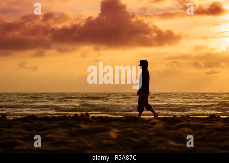 Homme marche et pense au coucher du soleil sur la plage Banque D'Images