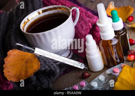 L'automne et les soins de santé. tasse de thé, pilules et thermomètre on a wooden background Banque D'Images