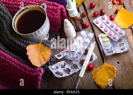 L'automne et les soins de santé. tasse de thé, pilules et thermomètre on a wooden background Banque D'Images
