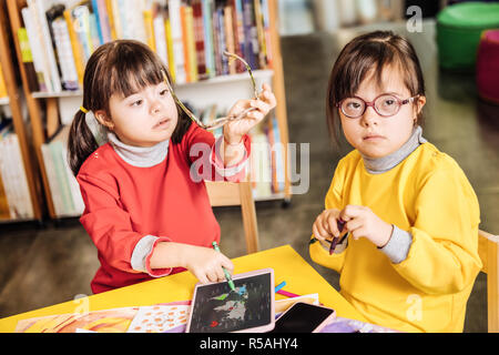 Près de sœur. Dark-eyed belle fille avec le syndrome de assis près de sa sœur en tenant lunettes Banque D'Images