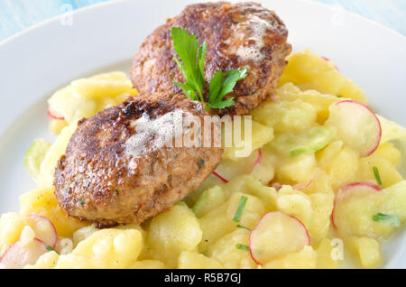 Des boulettes de boeuf de Bavière et le porc, frit dans une poêle de fer, servi sur salade de pomme de terre faite maison avec le concombre et radis Banque D'Images