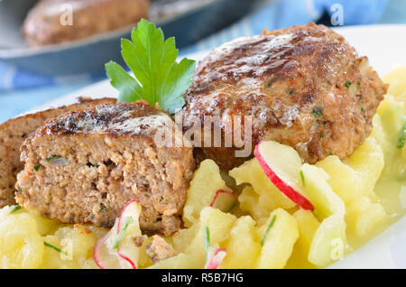 Des boulettes de boeuf de Bavière et le porc, frit dans une poêle de fer, servi sur salade de pomme de terre faite maison avec le concombre et radis Banque D'Images