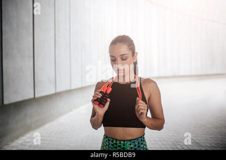 Attractive young woman in sports est uniforme et regarde vers le bas. Elle est titulaire d'orange corde autour du cou. Jeune femme est bon et bien construit. Elle a l'air awesom Banque D'Images