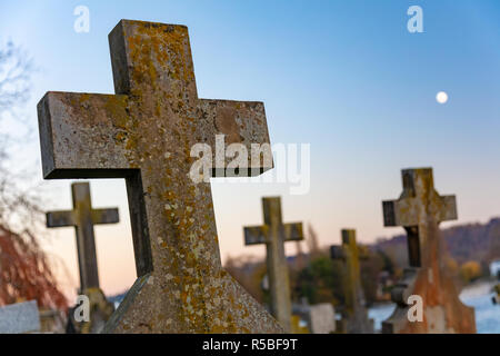 Pierres tombales croix Crucifix dans un cimetière de l'église avec une pleine lune dans un ciel du soir dans l'arrière-plan Banque D'Images