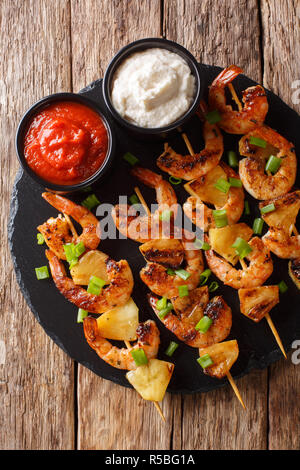 Brochettes de crevettes grillées à l'ananas frais et les oignons verts servis avec des sauces close-up sur une plaque en ardoise sur une table en bois. Haut Vertical voir fr Banque D'Images