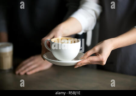 Close up of barista holding cappuccino aromatique, qui les servent de coffeeshop visiteur, serveuse qui tasse de café frais à la mousse de lait avec cafe g Banque D'Images